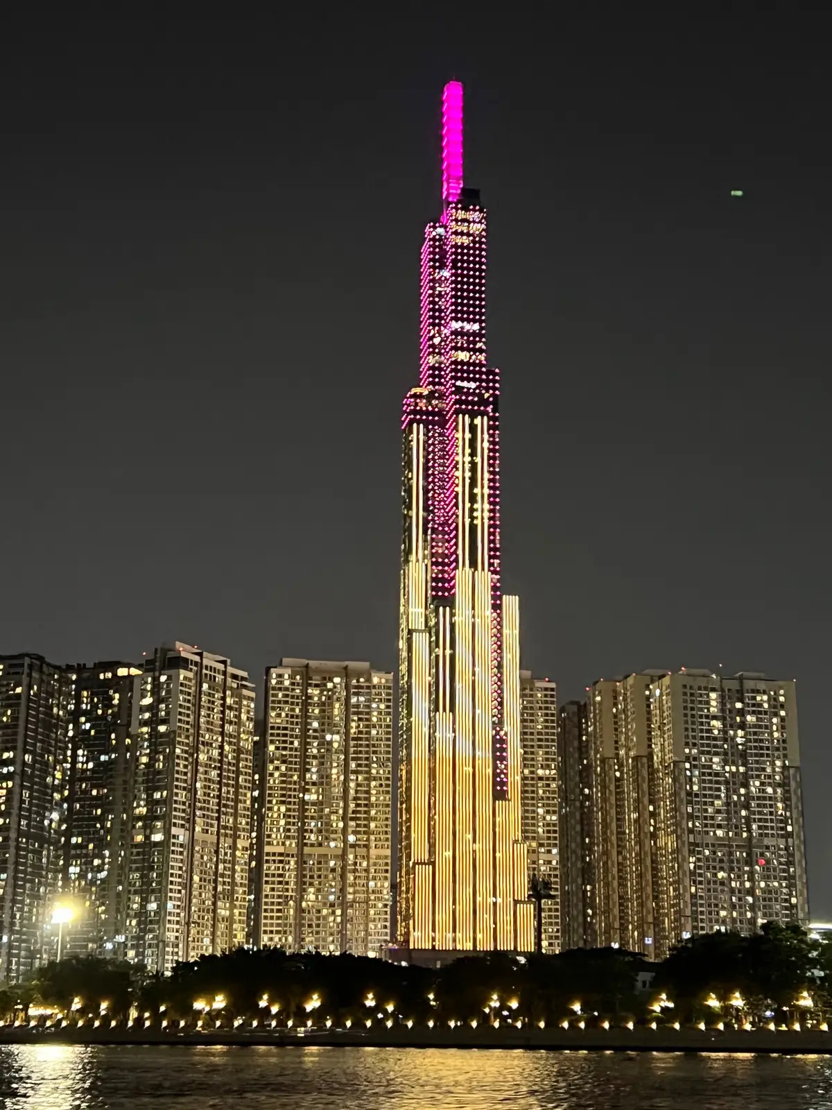 Tall lit tower with pink lights at night among apartment blocks
