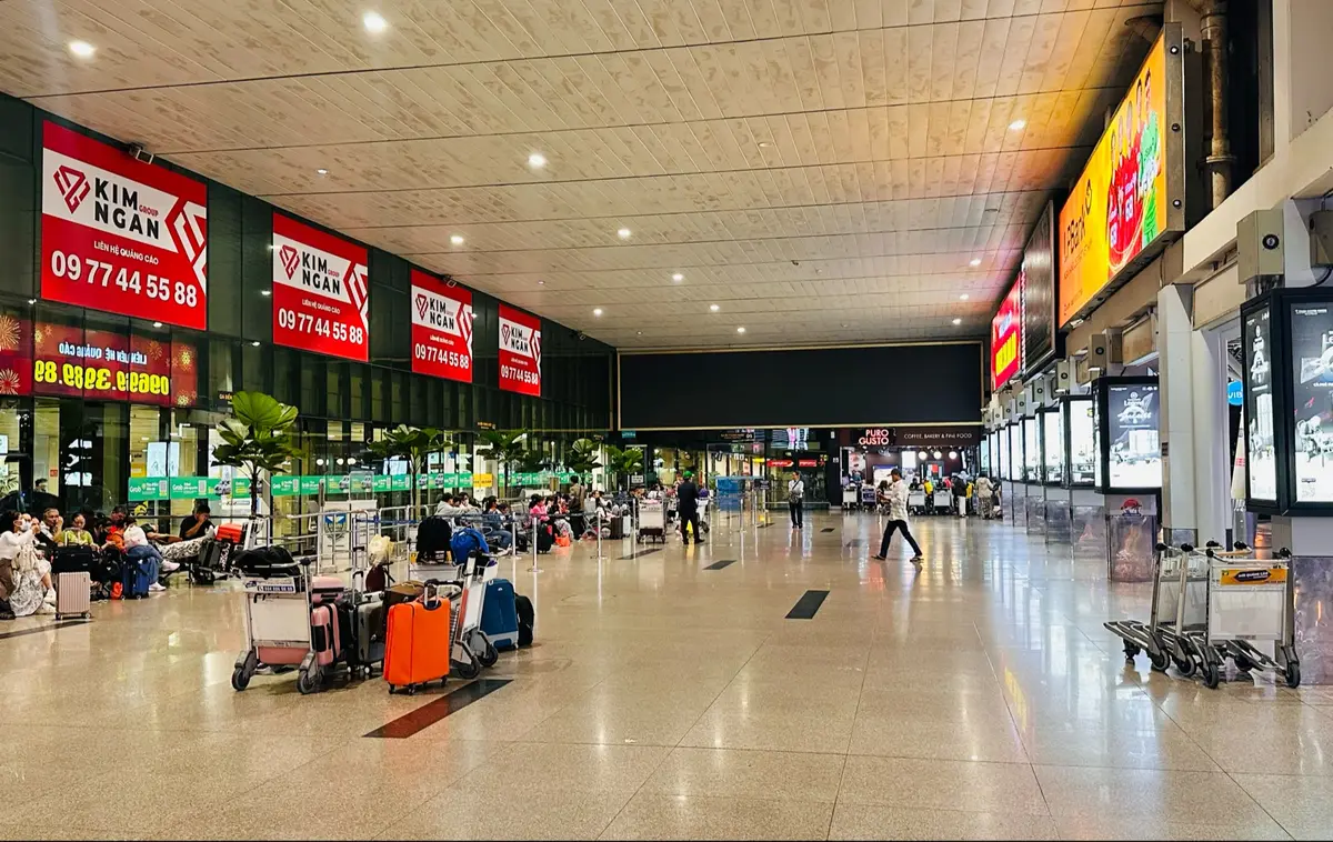 Long airport concourse with red advertising signs along the wall and travellers walking with luggage