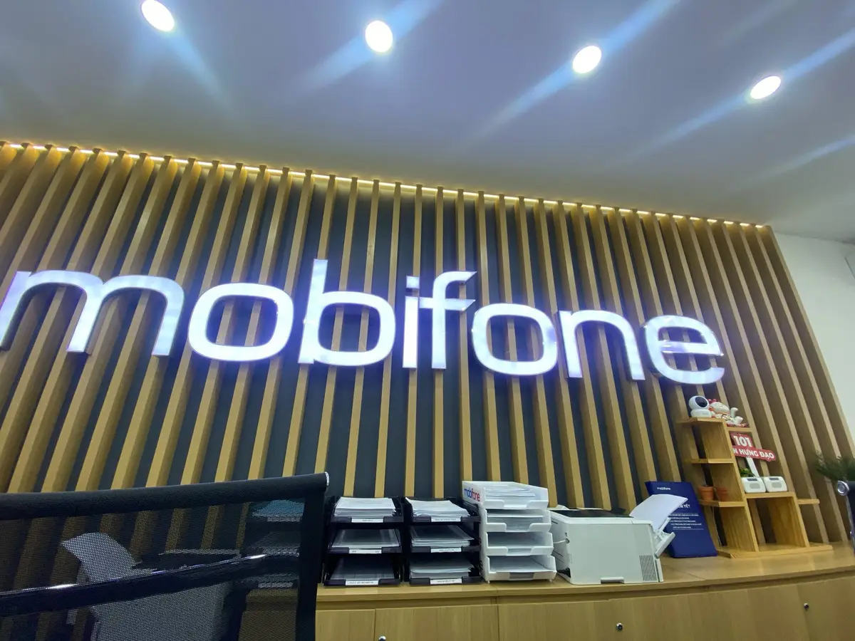 Counter inside the MobiFone store with the logo in lit letters on a wood-slat wall and a desk with papers