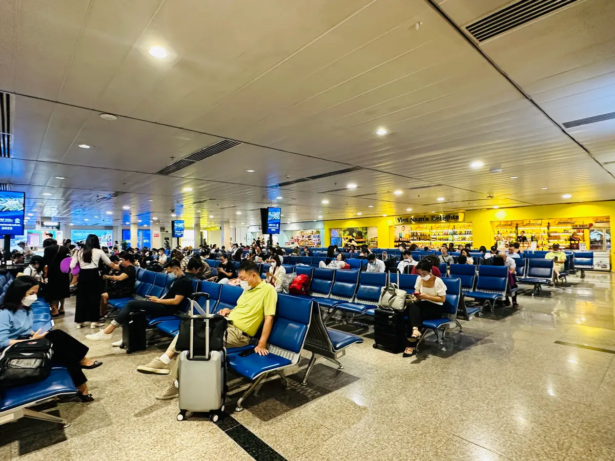 Rows of blue seats in a bright airport waiting hall with travellers and luggage