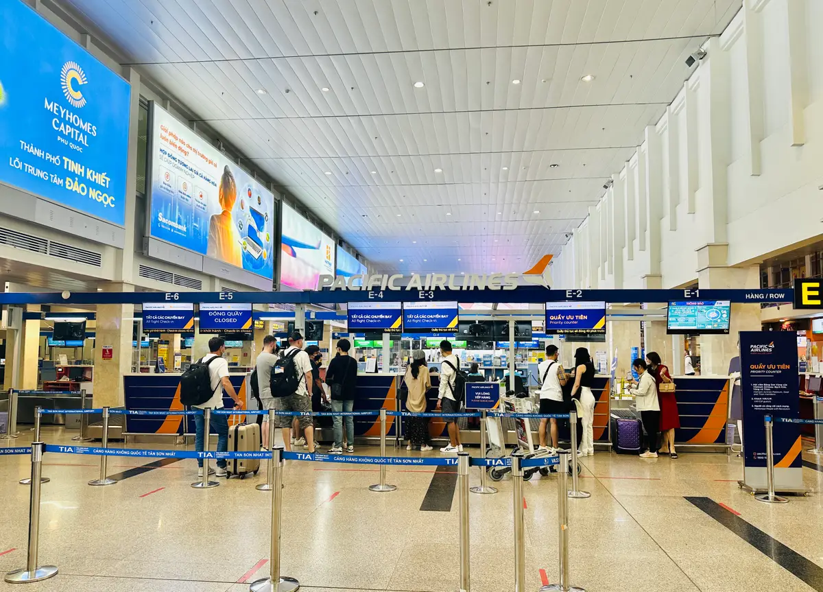 Check-in counters in an airport hall with queue barriers and travellers waiting at the desks