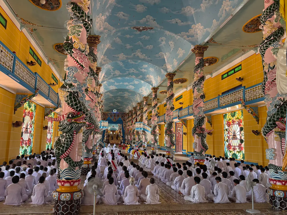 Worshippers in white robes seated in rows inside a hall with dragon-wrapped pillars and a painted sky ceiling