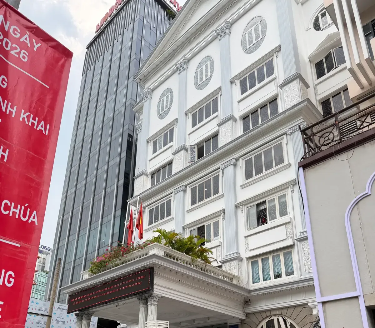 Upper floors of a white multi-storey office building with columns, balconies and flags, seen from the street.
