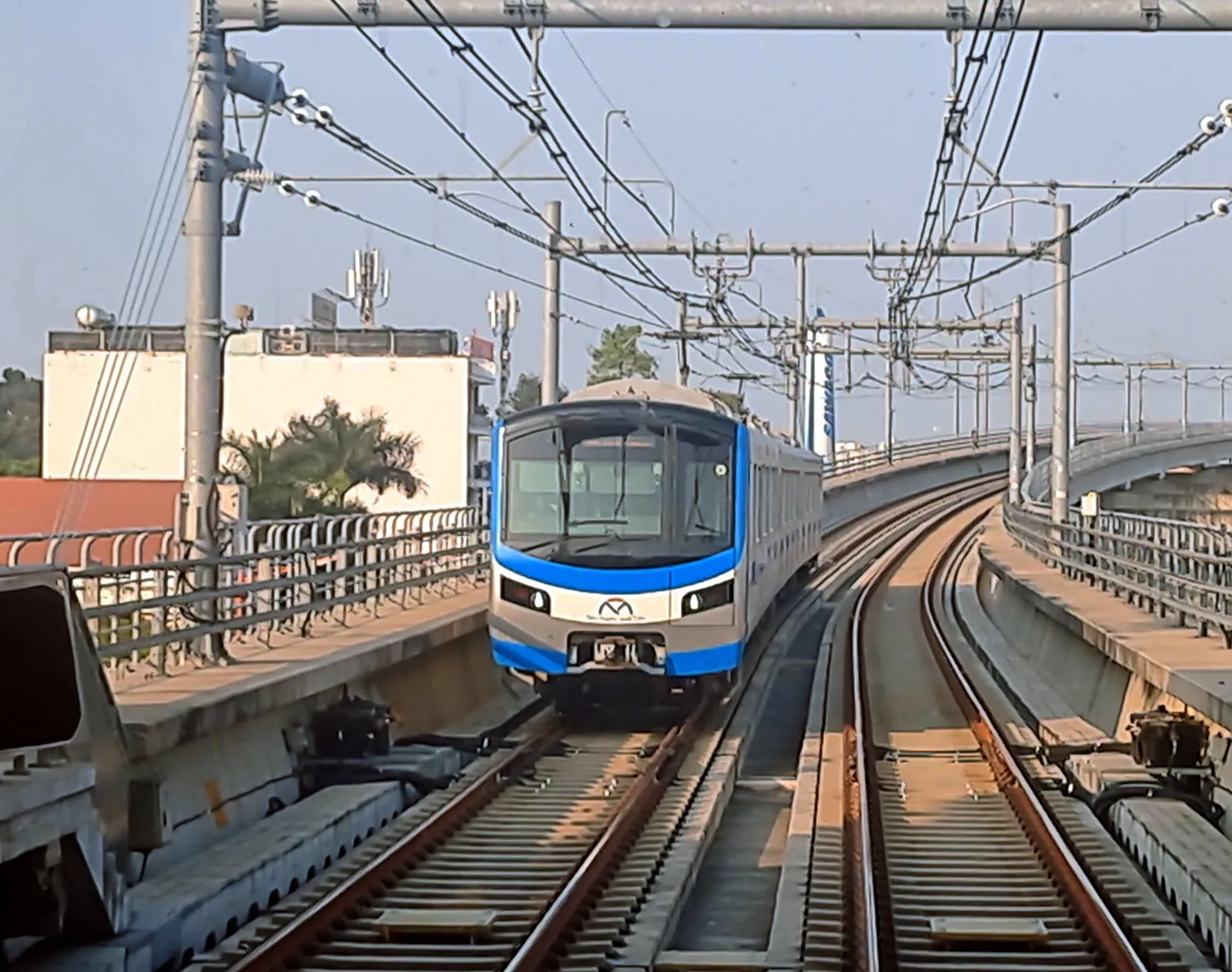 Blue and grey metro train approaching on an elevated track with overhead cables