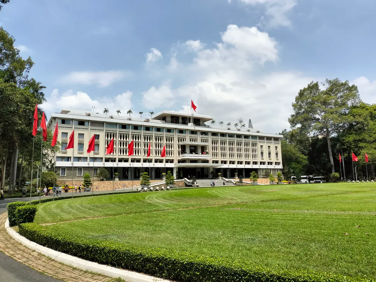 White modernist palace building with red flags behind a curved lawn on a sunny day