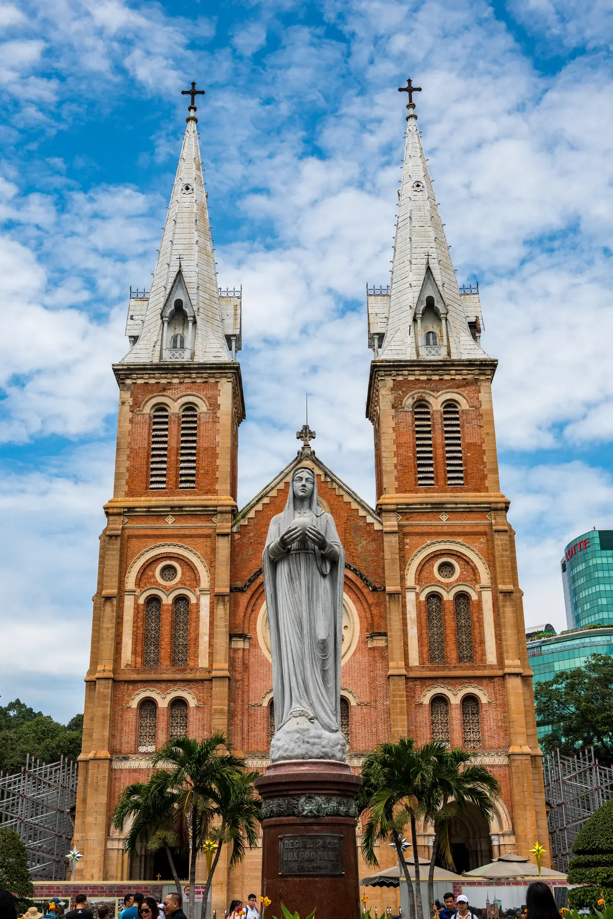 Twin red-brick bell towers and a white statue of the Virgin Mary in front of the cathedral under a blue sky