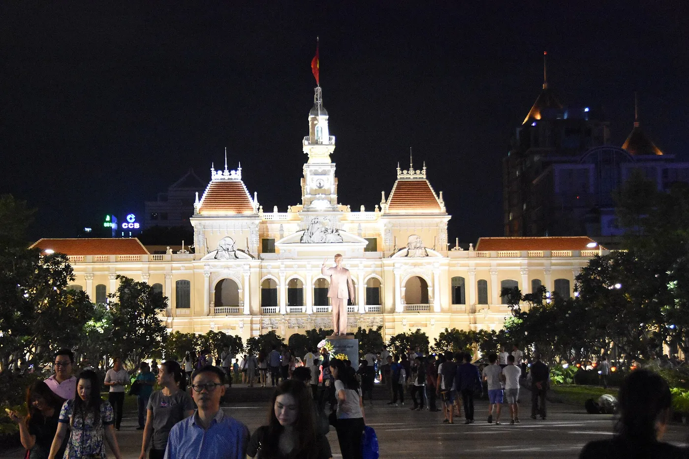 Floodlit French colonial city hall building at night with people gathered in the plaza in front