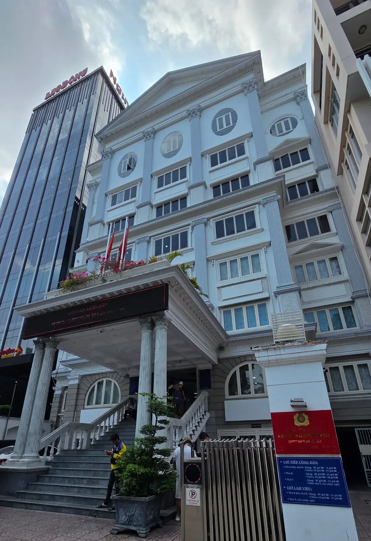 Front of a white multi-storey office building with columns, a porch, flags and a metal gate.
