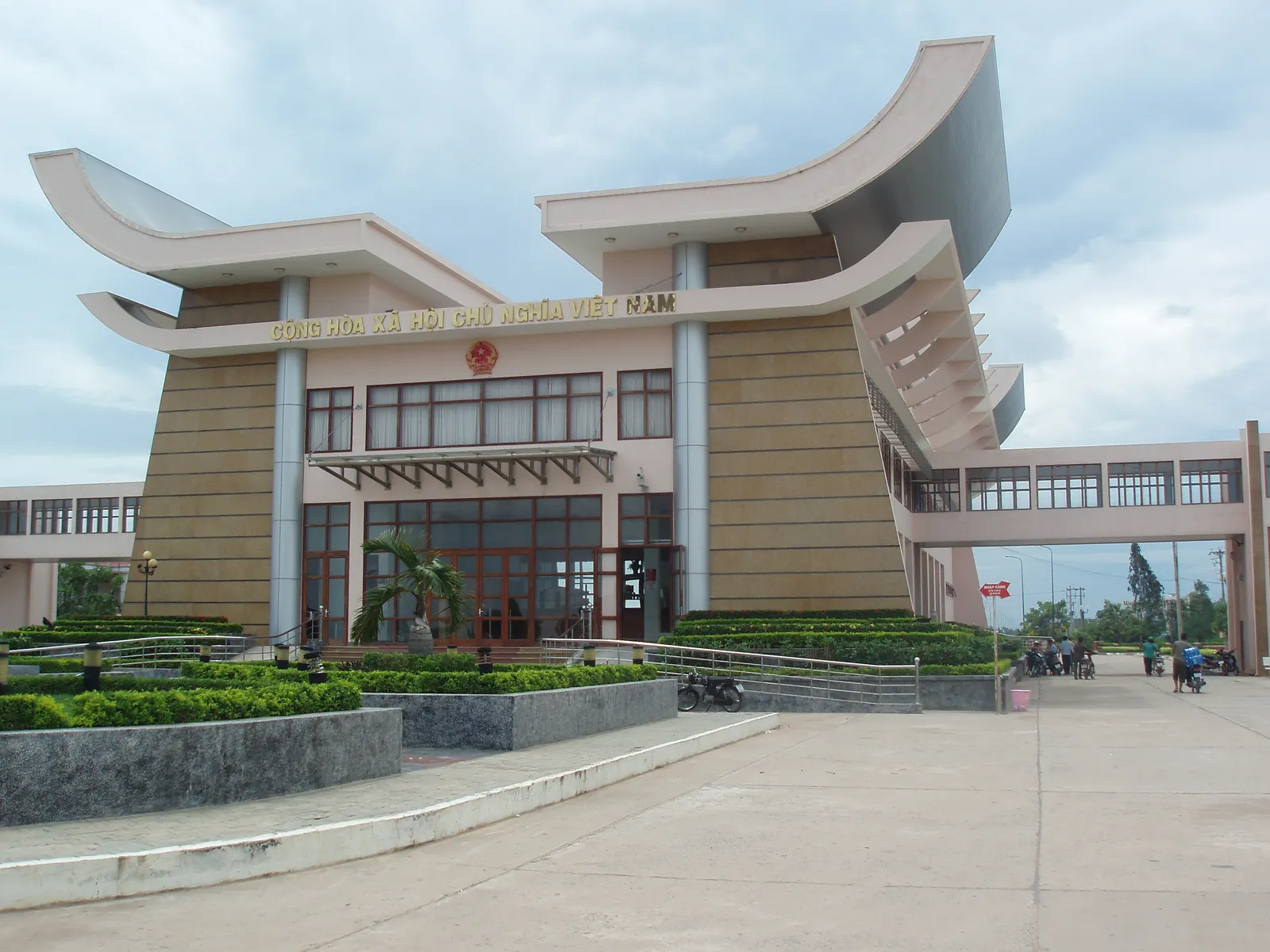 Large border building at Moc Bai with swept roof edges, glass doors and a covered walkway beside lawns