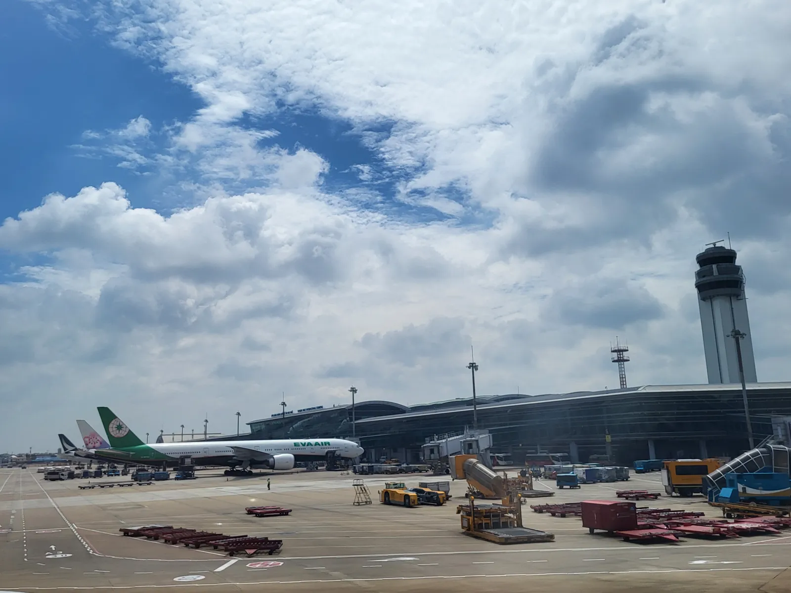 Aircraft parked on the apron at Tan Son Nhat Airport in front of the terminal building and control tower under a cloudy sky