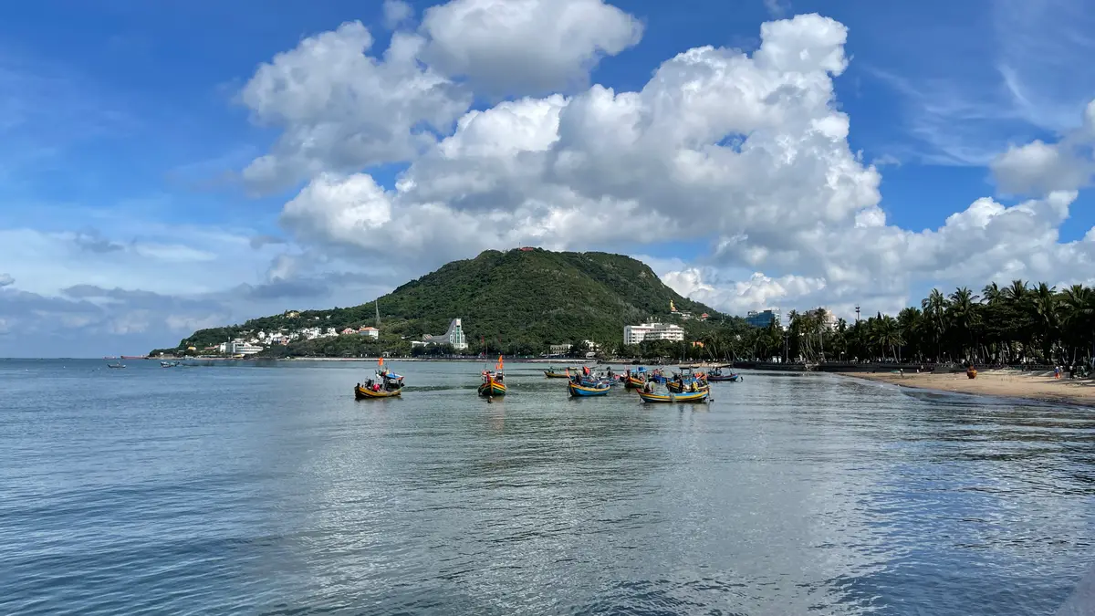 Fishing boats on calm water with a green hill and white clouds behind