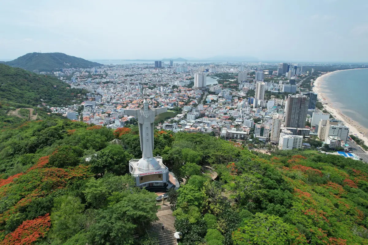 White statue on a green hill with the city and beach spread out below