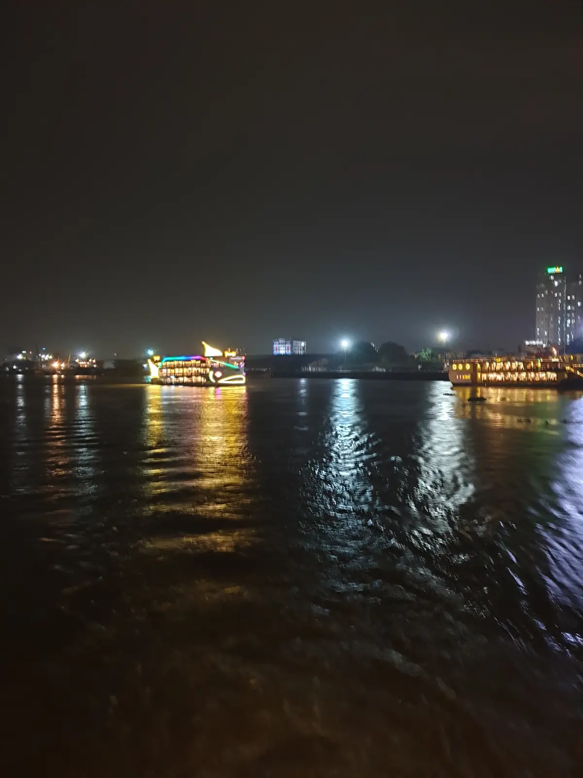 Lit boats and city lights across the dark river at night