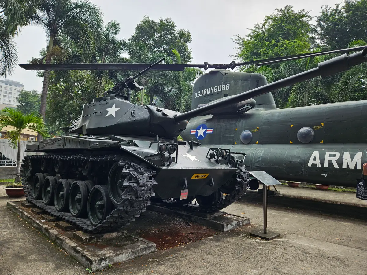 Tracked light tank with a gun turret displayed on a paved yard beside other military vehicles