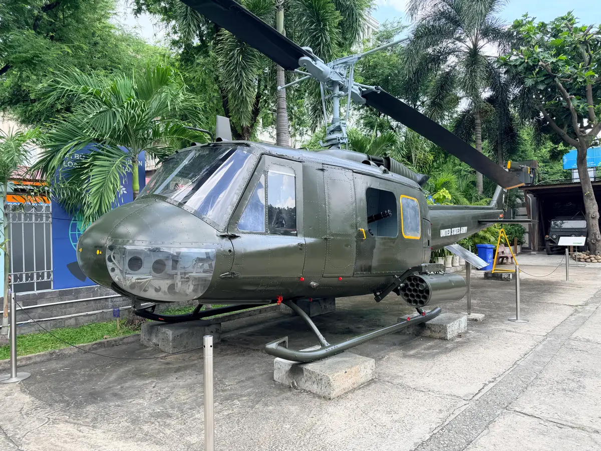Olive green military helicopter parked outdoors among palm trees